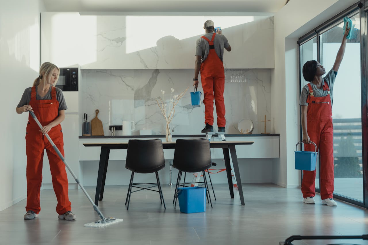 services-01 Group of cleaners in red uniforms mopping and wiping glass in a modern dining room.