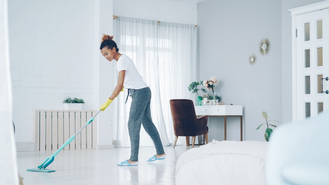 services-03 Pretty African American girl is mopping floor at home with flat plastic mop wearing gloves and wear-at-home clothing. Modern interiors, cleanness and young people concept.