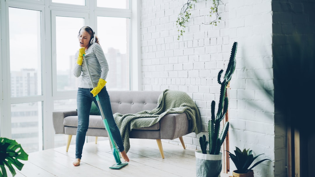 gallery-1 Happy young housewife is dancing and singing during housecleaning, she is listening to music in headphones and mopping floor having fun. Housework and technology concept.