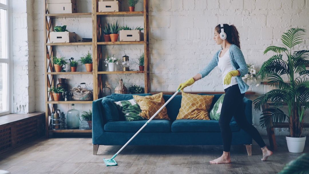 gallery-3 Cheerful young woman is dancing with mop during routine clean-up in nice loft style apartment, she is listening to music with wireless headphones and singing enjoying her occupation.