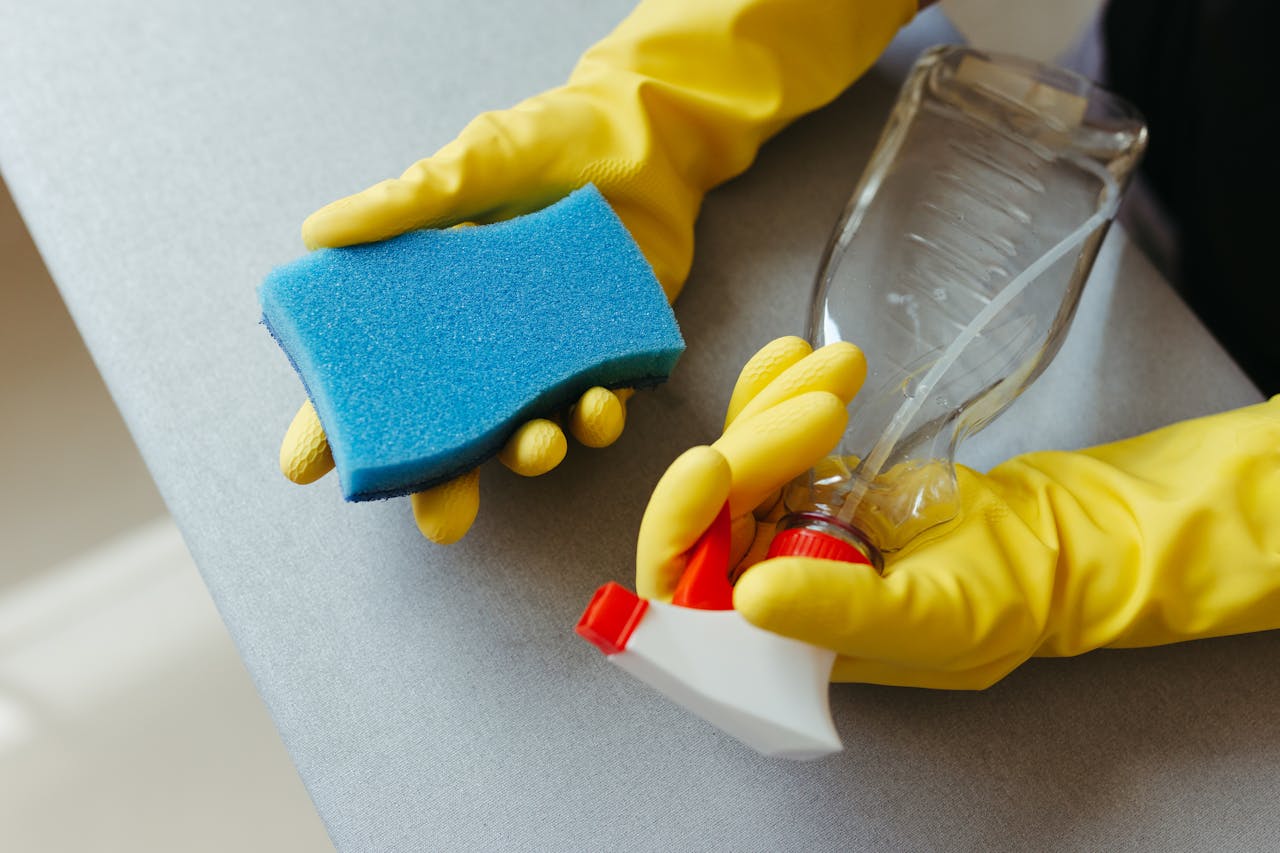 hero-img-01 Close-up of hands in gloves holding a sponge and spray bottle for cleaning.