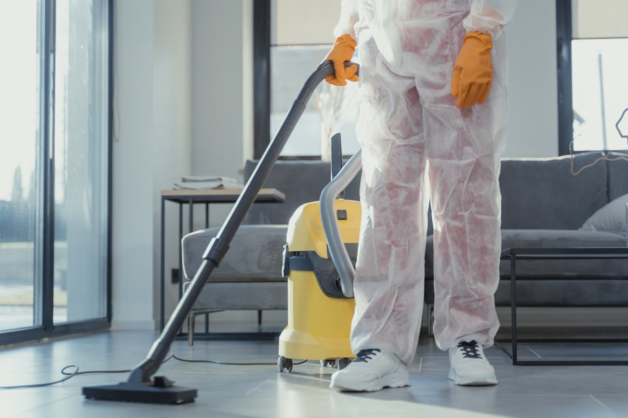 hero-img-02 A cleaner in protective coveralls and gloves vacuuming a modern living room.